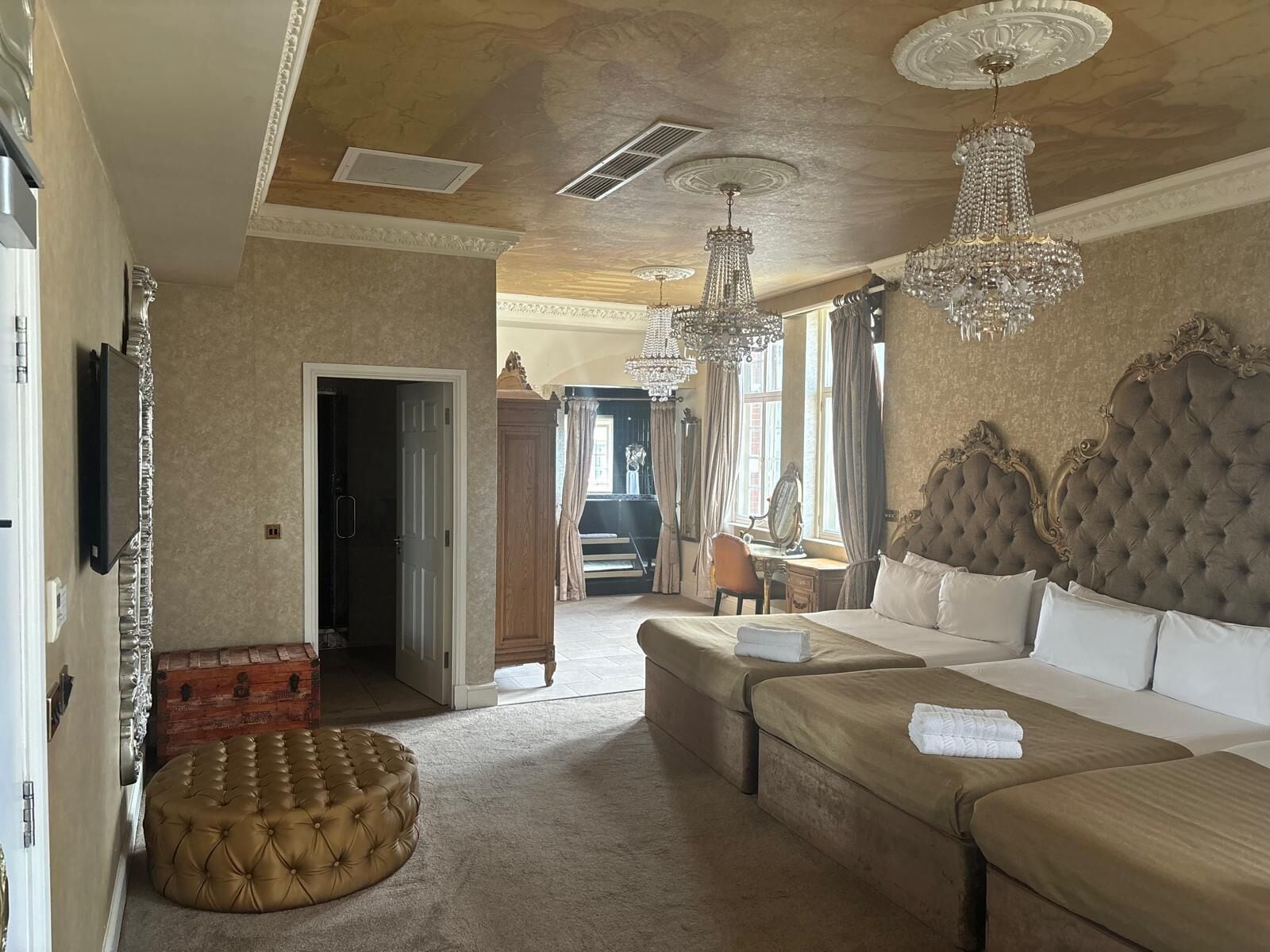 A luxurious bedroom with a large bed, a chaise lounge, and a tufted ottoman.