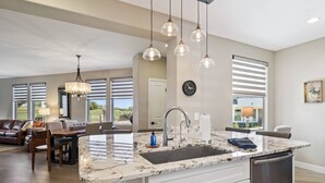 A spacious kitchen with a marble countertop, stainless steel sink, and modern pendant lights.