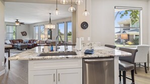 A spacious living area with a large kitchen island, modern pendant lights, and a view of the outdoors.
