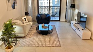 Een moderne woonkamer met een bank, een ronde salontafel, een televisie en een balkon met uitzicht op gebouwen.
