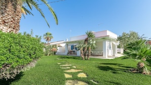 Une maison moderne à l’extérieur blanc, dotée d’un patio couvert et d’une pelouse bien entretenue agrémentée de palmiers.