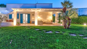 Une maison moderne dotée d’un patio couvert, d’un coin repas et d’une pelouse bien entretenue.