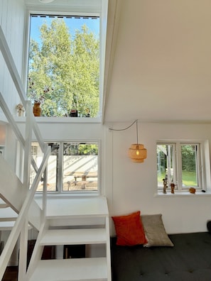 Una habitación con escalera, un sofá y dos ventanas que dan a árboles.