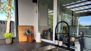 Une cuisine avec une grande fenêtre, une planche à découper en bois, un porte-couteaux et un évier.