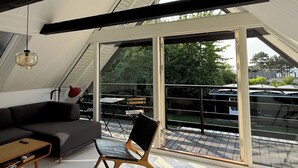 Une chambre de style loft moderne, avec un plafond en pente, de grandes fenêtres, un canapé, un fauteuil et une table.