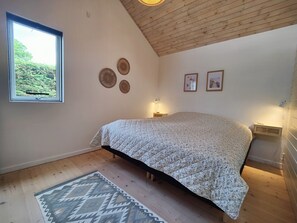 A bedroom with a bed, a window, a wall-mounted air conditioner, and a patterned rug.
