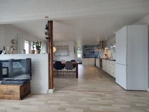 A spacious kitchen with white cabinets, a dining area with a wooden table and chairs, and a television on a wooden crate.
