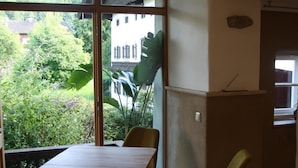 A dining area with a table and chairs, a kitchen area with a stove, and a view of greenery outside. - Vacation apartment with terrace and mountain view (Frasdorf)