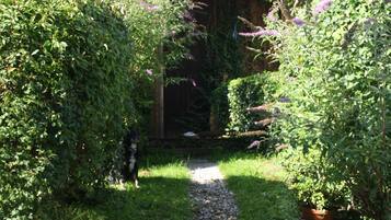 Ein Weg führt zu einem Gebäude mit überdachter Veranda, umgeben von üppigem Grün und blühenden Pflanzen.