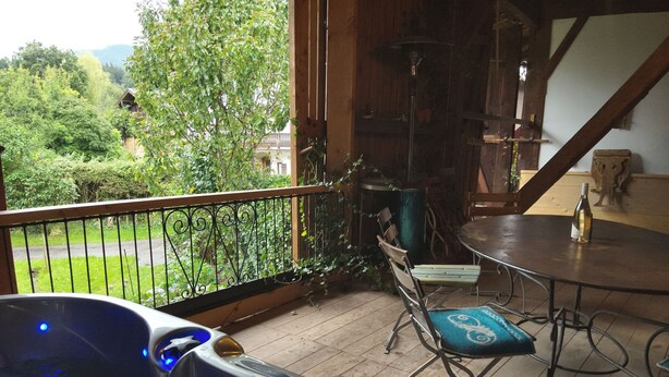 A hot tub with a view of a balcony, a dining table with chairs, and a wooden staircase. - Vacation apartment with terrace and mountain view (Frasdorf)