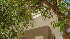 Un espacio exterior moderno con un edificio color beige, una puerta blanca y una zona de estar con sillas y una mesa.