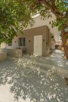 A modern outdoor area with a beige building, a white door, and a seating area with chairs and a table.
