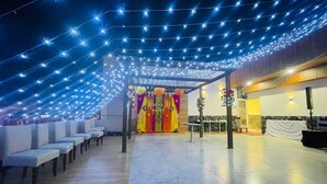 Un salón amplio con filas de sillas blancas, un escenario con cortinas coloridas y luces colgantes.