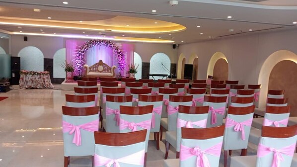 A conference room with rows of chairs, a stage with floral decorations, and a white backdrop. - Hotel Star Suites By Star Group (New Delhi)