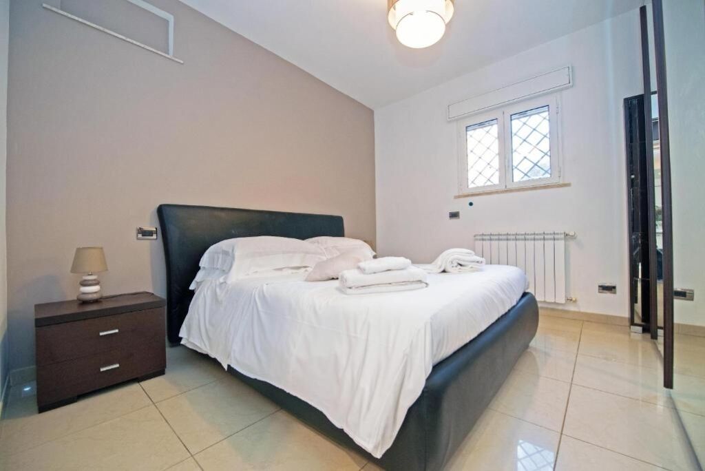 A bedroom with a bed, a nightstand, a lamp, and a window.
