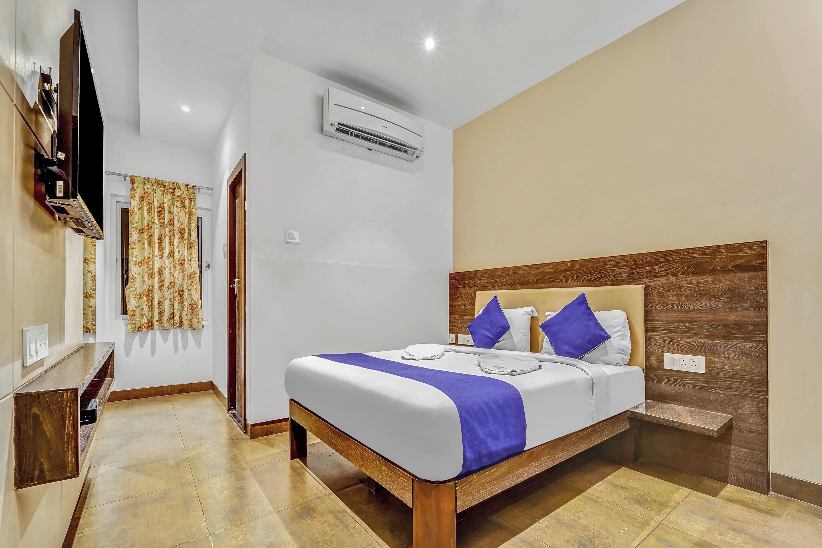 A hotel room with a bed, a TV, an air conditioner, and a wooden headboard.