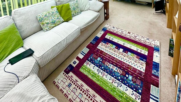 A conservatory with a white sofa, green cushions, and a colorful quilt on the floor. - Glendale close - Huku Kwetu - 4 Bedroom (Nottingham)
