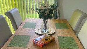 A wooden dining table with two green placemats, a vase with white flowers, and a box of cookies. - Glendale close - Huku Kwetu - 4 Bedroom (Nottingham)