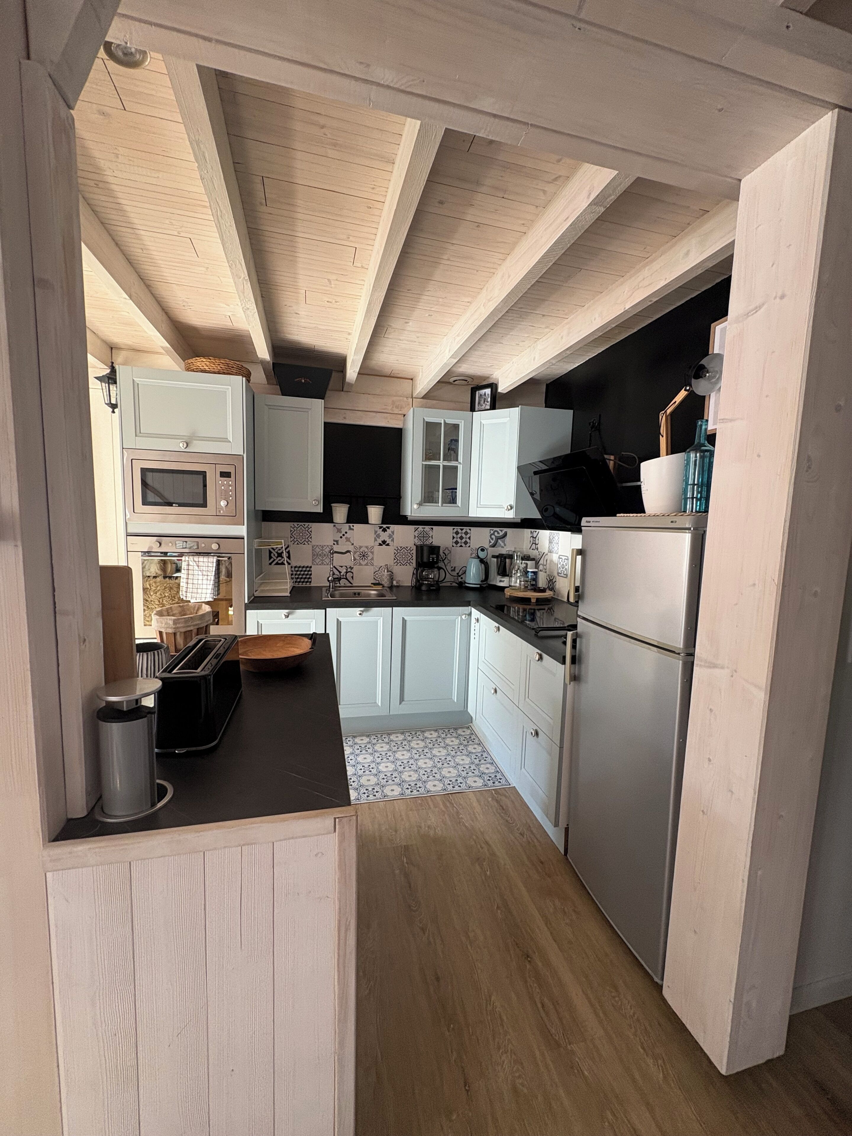 A kitchen with wooden beams, white cabinets, a microwave, a toaster, and a refrigerator.