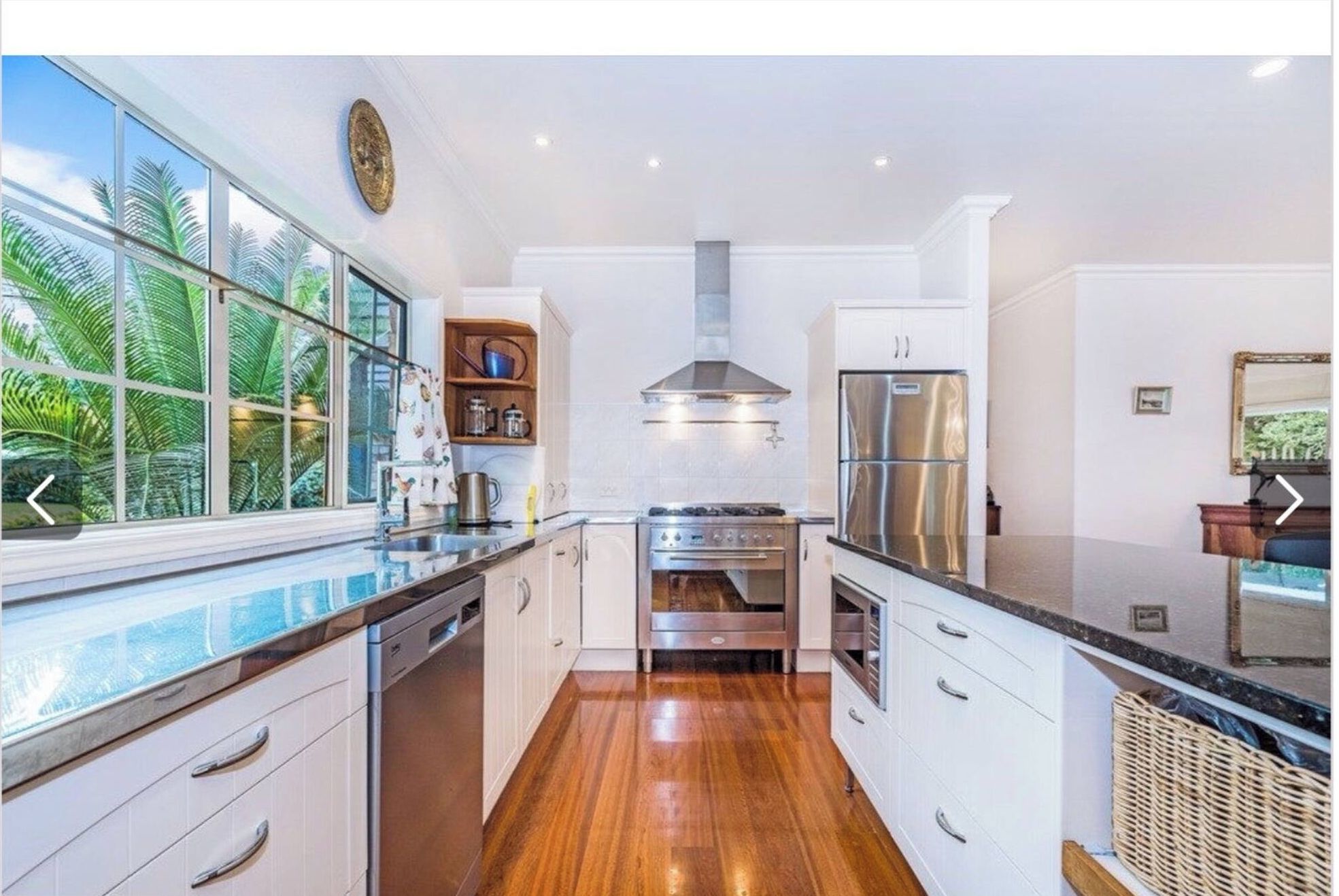 A modern kitchen with white cabinets, stainless steel appliances, and a wooden floor.