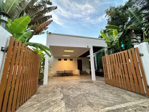 A modern building with a covered patio area, wooden gates, and lush greenery.
