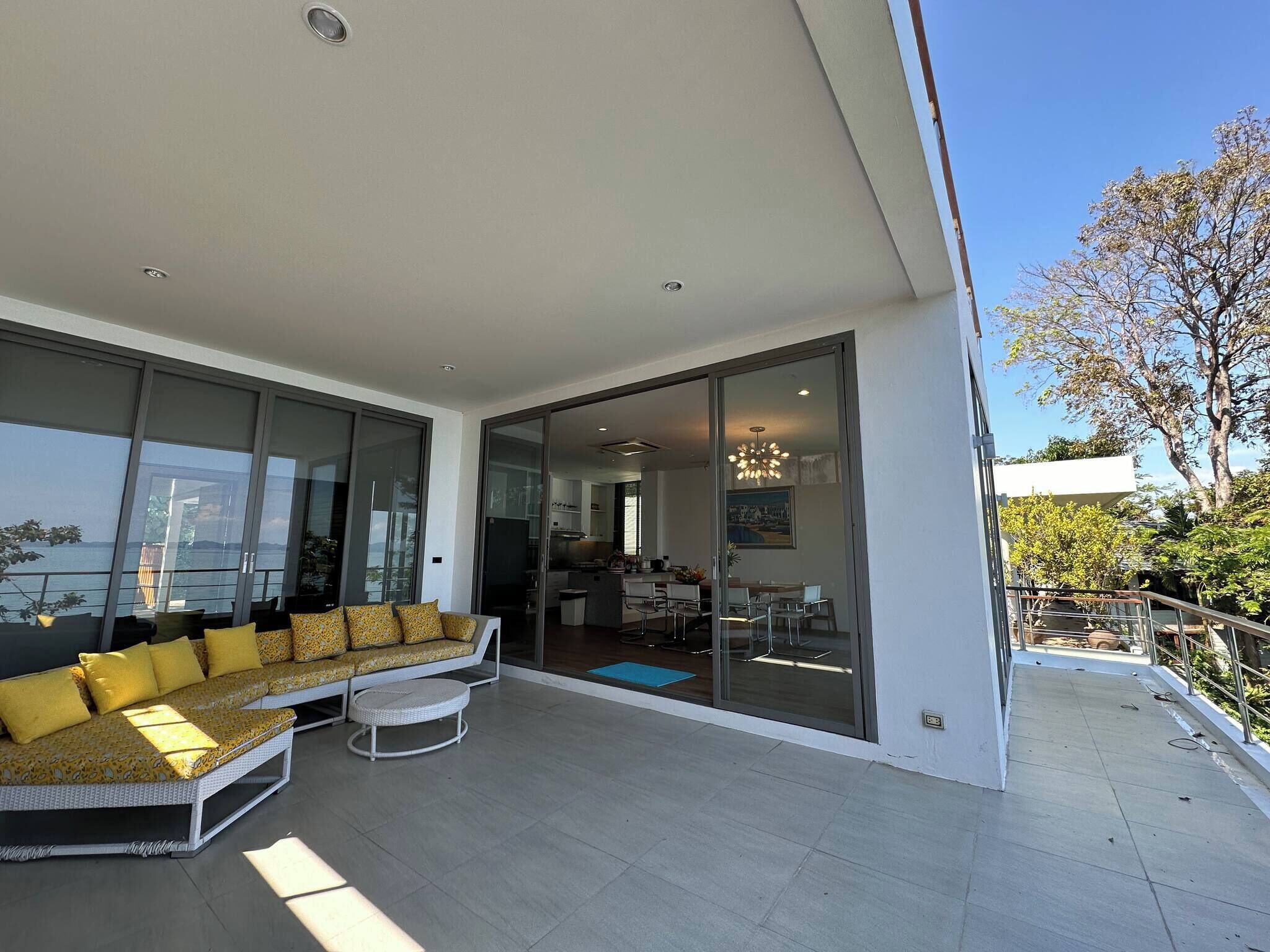 A modern living room with a sofa and a dining area, large glass doors leading to a kitchen and dining space, and a view of the sea.