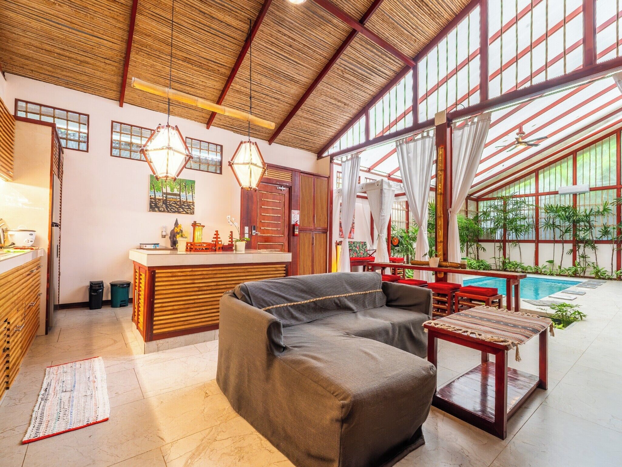 A spacious room with a large sofa, a wooden counter, and a pool area.