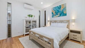 Une chambre à coucher avec un lit en bois, des tables de chevet blanches, une armoire blanche et un grand tableau abstrait accroché au mur.