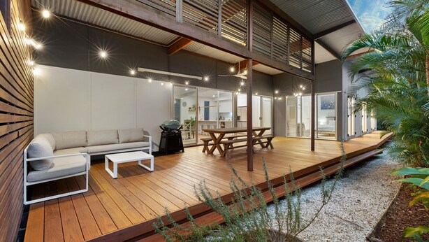 Un espace de vie extérieur moderne, doté d’une terrasse en bois, d’un canapé, d’une table et d’un barbecue.
