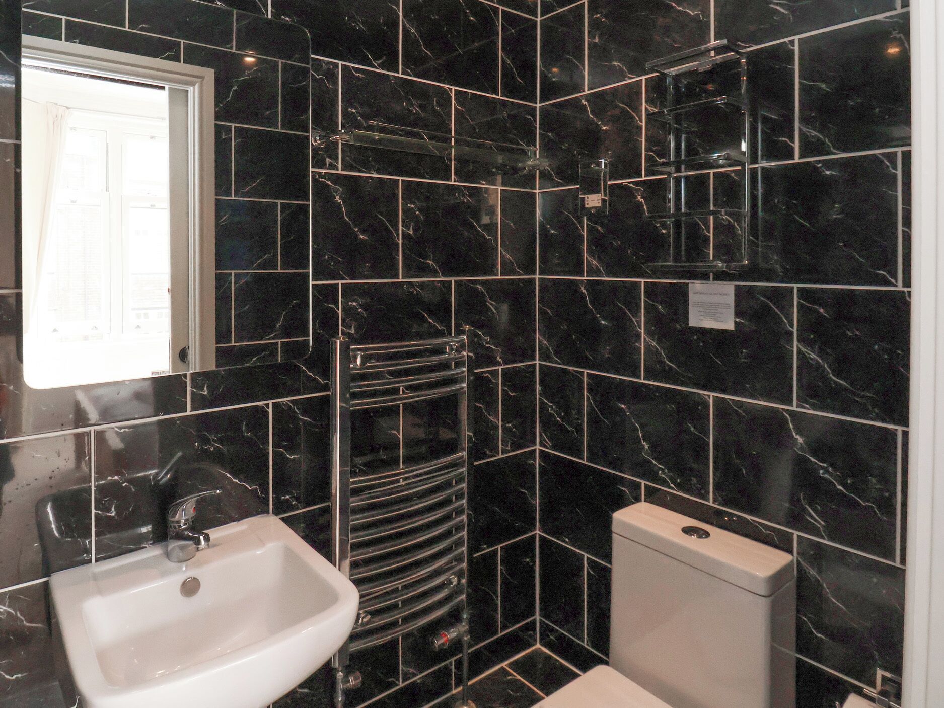Casa de banho com azulejos de mármore preto, uma pia branca, um porta-toalhas e uma sanita.