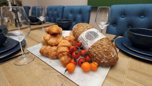 A table set with bread, croissants, and cherry tomatoes, with a wine glass and bowls on a wooden table. - All Seasons (Filey)