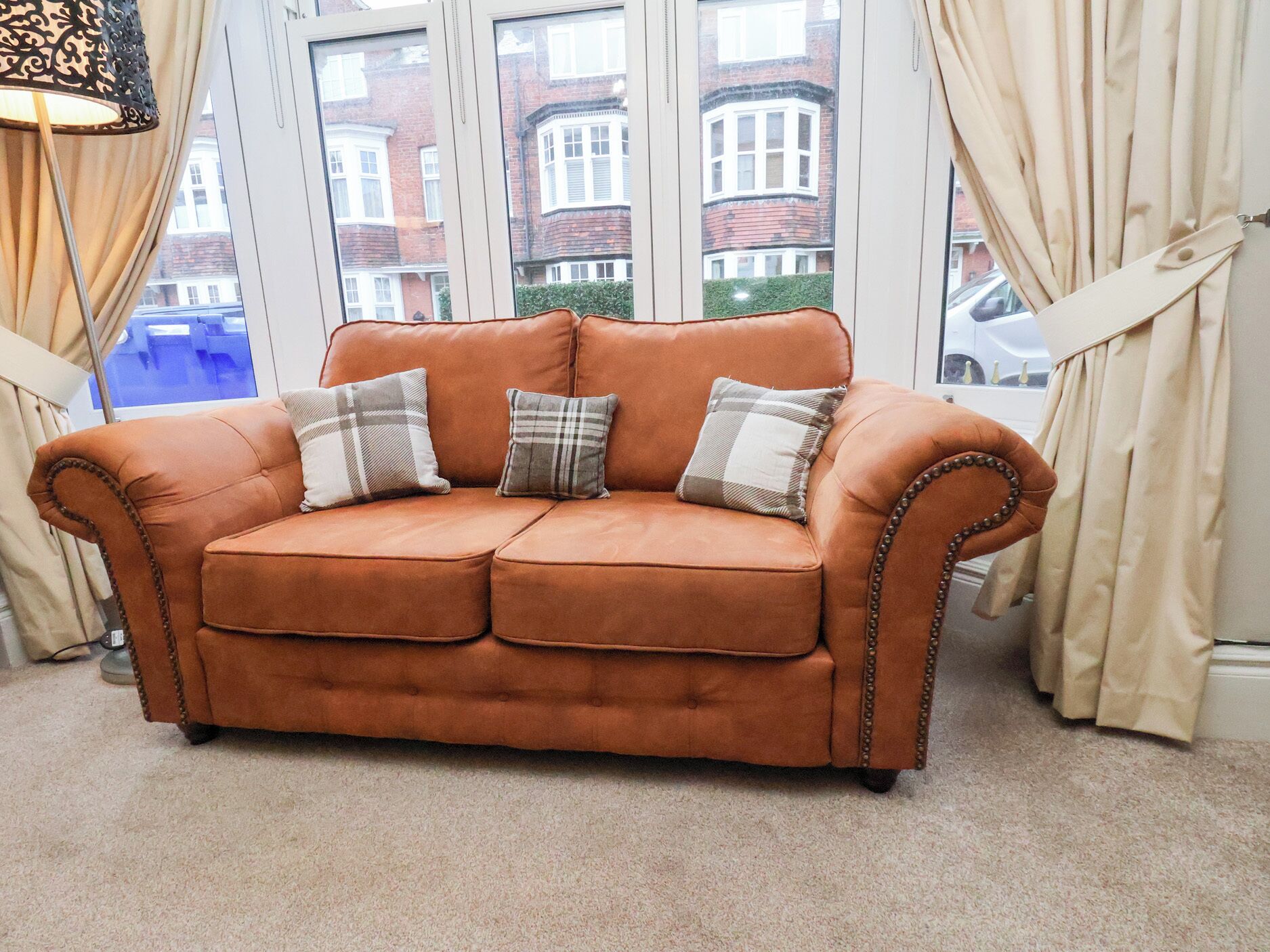 A brown leather sofa with three cushions, positioned in front of a window with curtains.