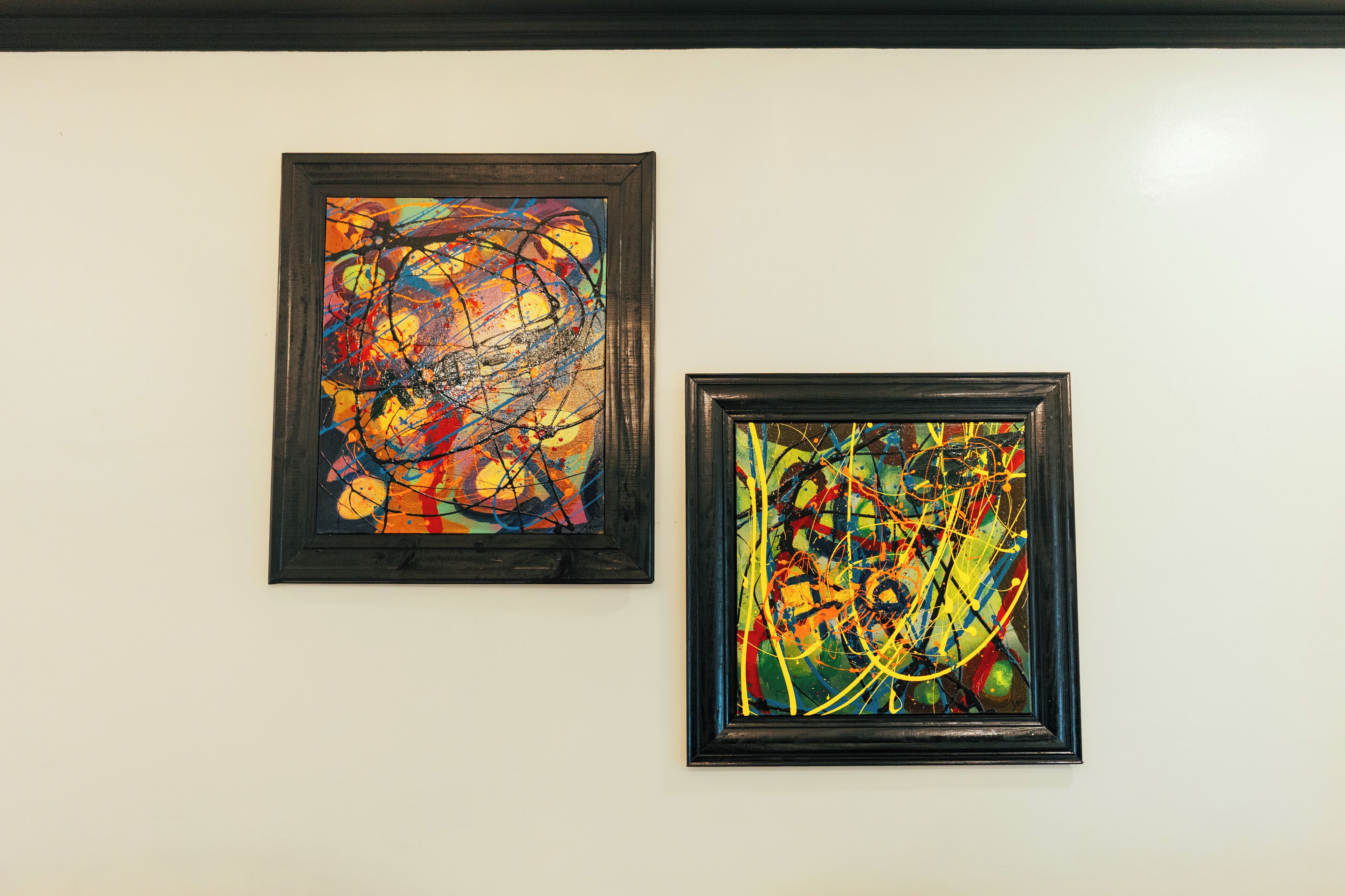 Two framed abstract paintings on a white wall.