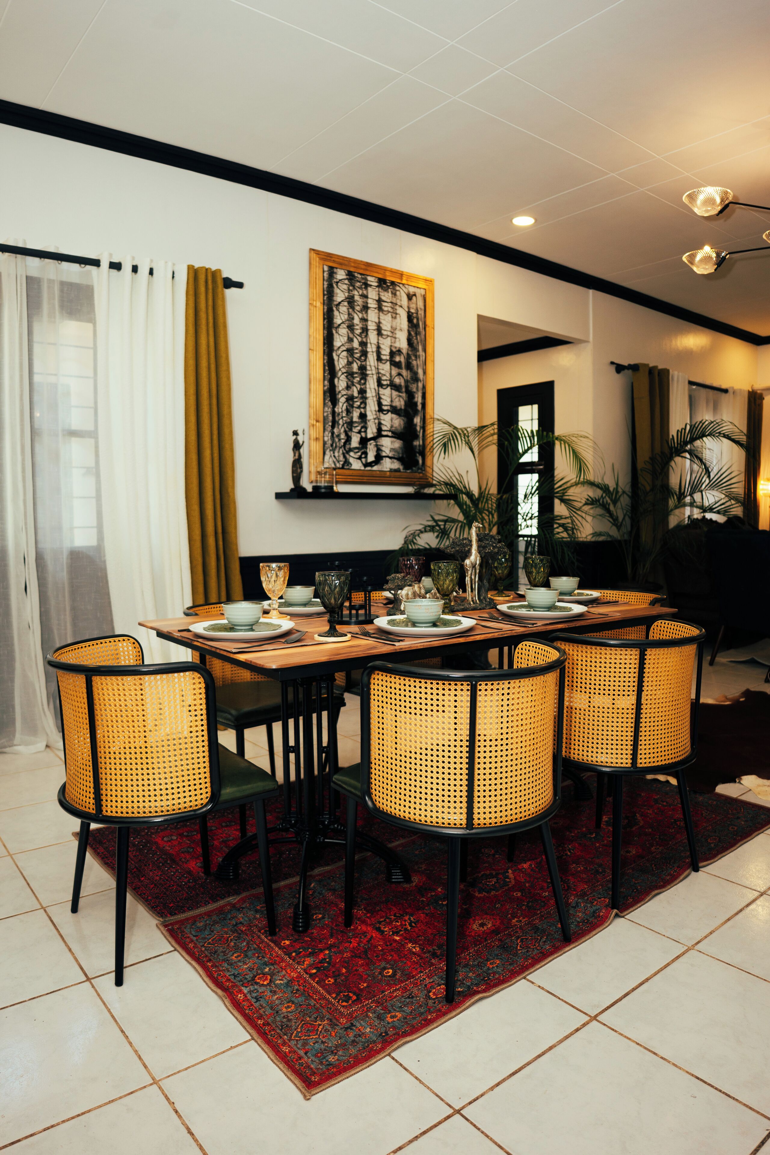 A dining area with a wooden table, wicker chairs, and a red patterned rug.