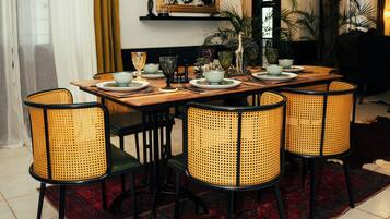 A dining area with a wooden table, wicker chairs, and a red patterned rug.