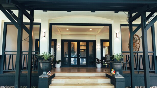 A covered entrance with a wooden staircase leading to a dark interior, flanked by potted plants and a decorative wall piece. - Casa Dela Tierra by Araw Residences (Mambajao)