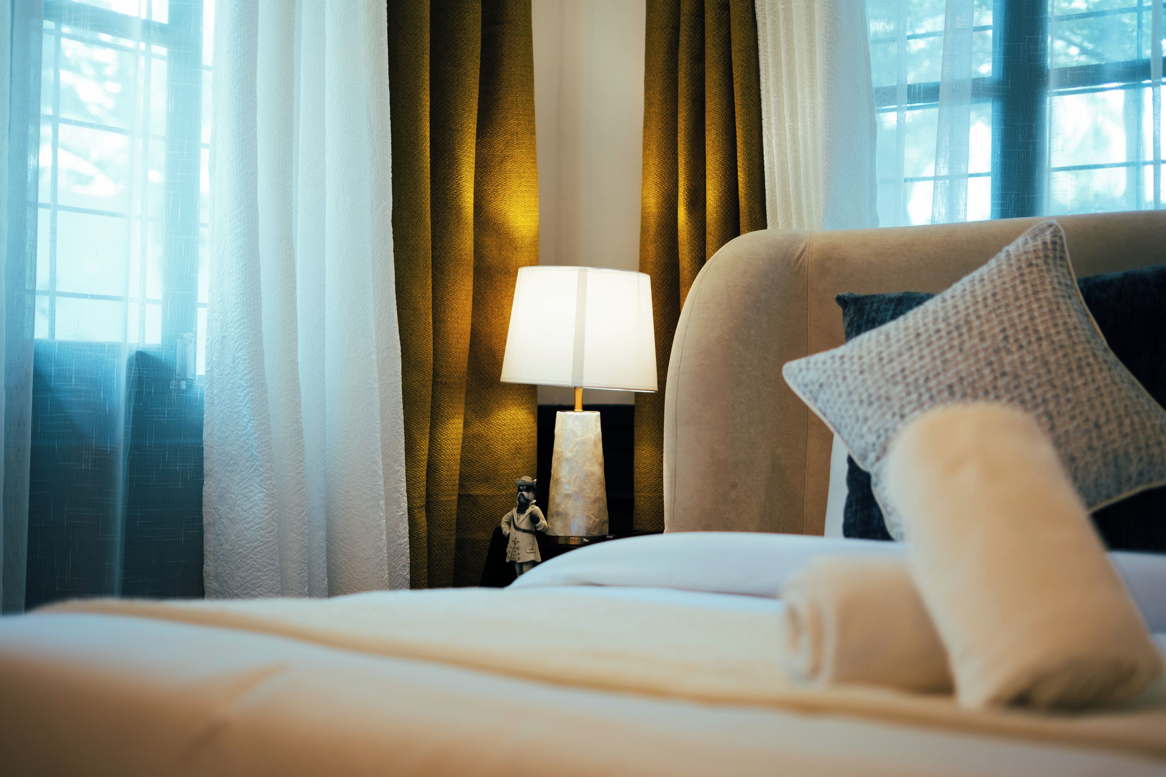 A neatly made bed with a rolled towel and pillows, a bedside lamp, and a small statue on a nightstand.