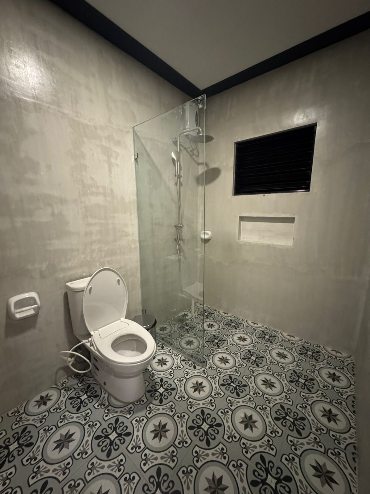 Ein Badezimmer mit Toilette, einer Duschkabine und Fliesen mit Muster.
