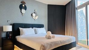 A modern hotel room with a large bed, a bedside table with a lamp, and a view of the city through the window.