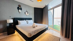 Une chambre d’hôtel moderne, dotée d’un grand lit, d’une table de chevet avec une lampe, d’une horloge murale et offrant une vue sur l’extérieur grâce à une grande fenêtre.