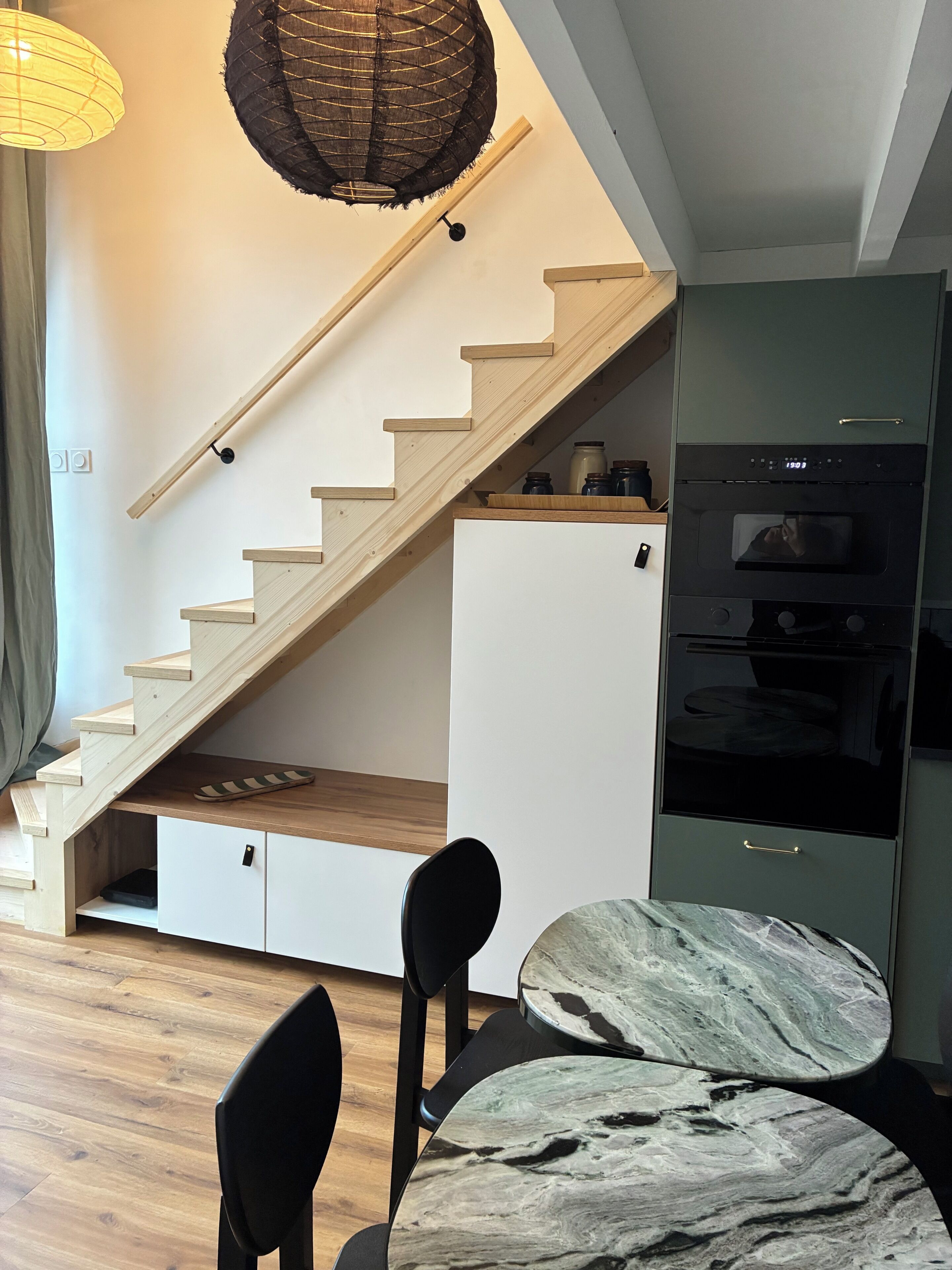 Een moderne keuken met een ingebouwde oven, een houten trap en een eethoek met een marmeren tafel.