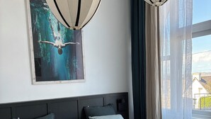 A hotel room with a large bed, two pillows, a blanket, a painting on the wall, and a window with curtains. - 3* Apartment for 2–4 people, 25 m² terrace—50 m from the beach and the GR34 trail. Dogs Welcome (Carantec)