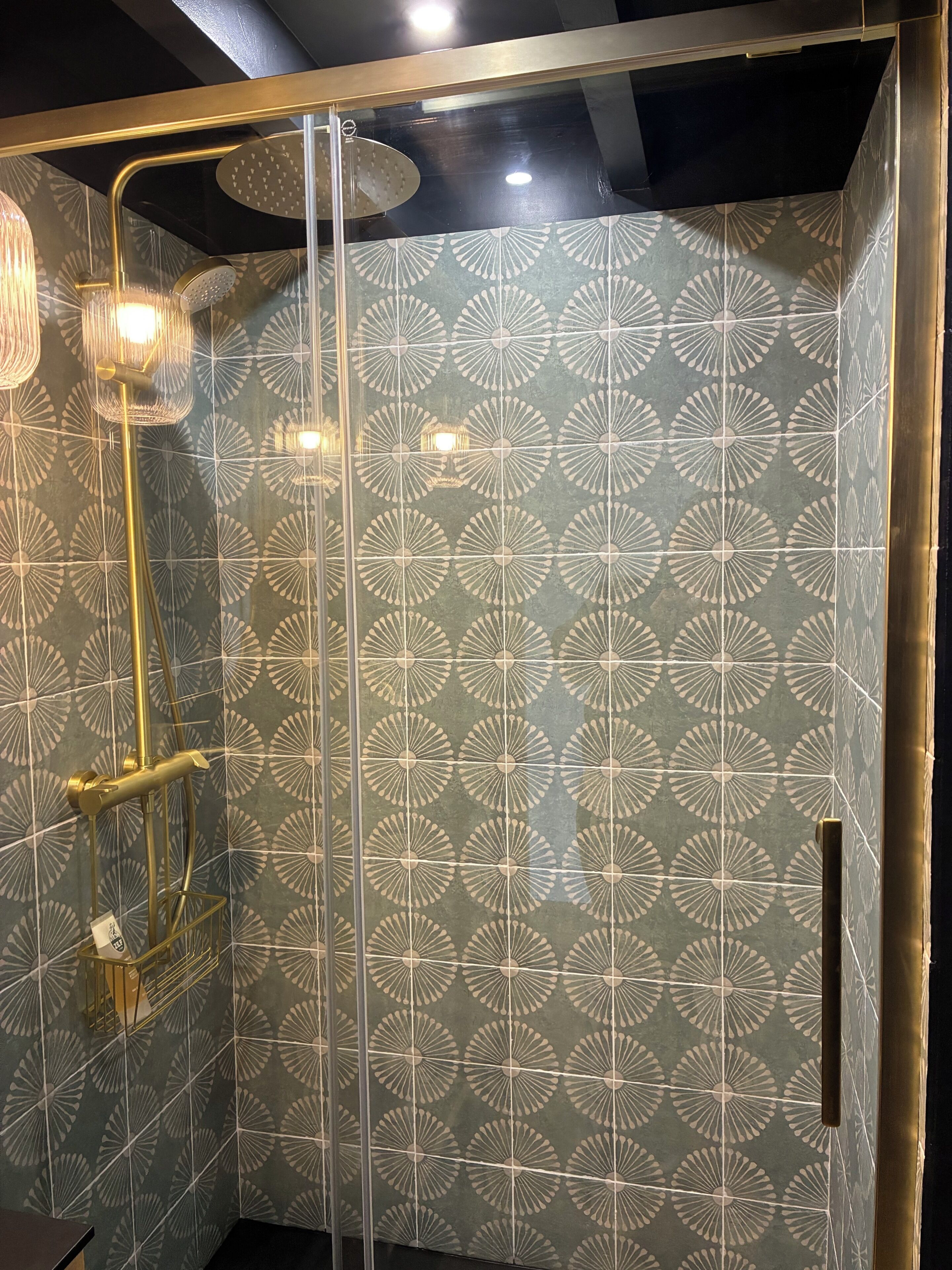 Een douche met een gouden frame, een glazen deur en een behang met een patroon.