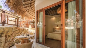 Una habitación con cama, puerta de vidrio, silla de mimbre y una mesa con superficie de vidrio.