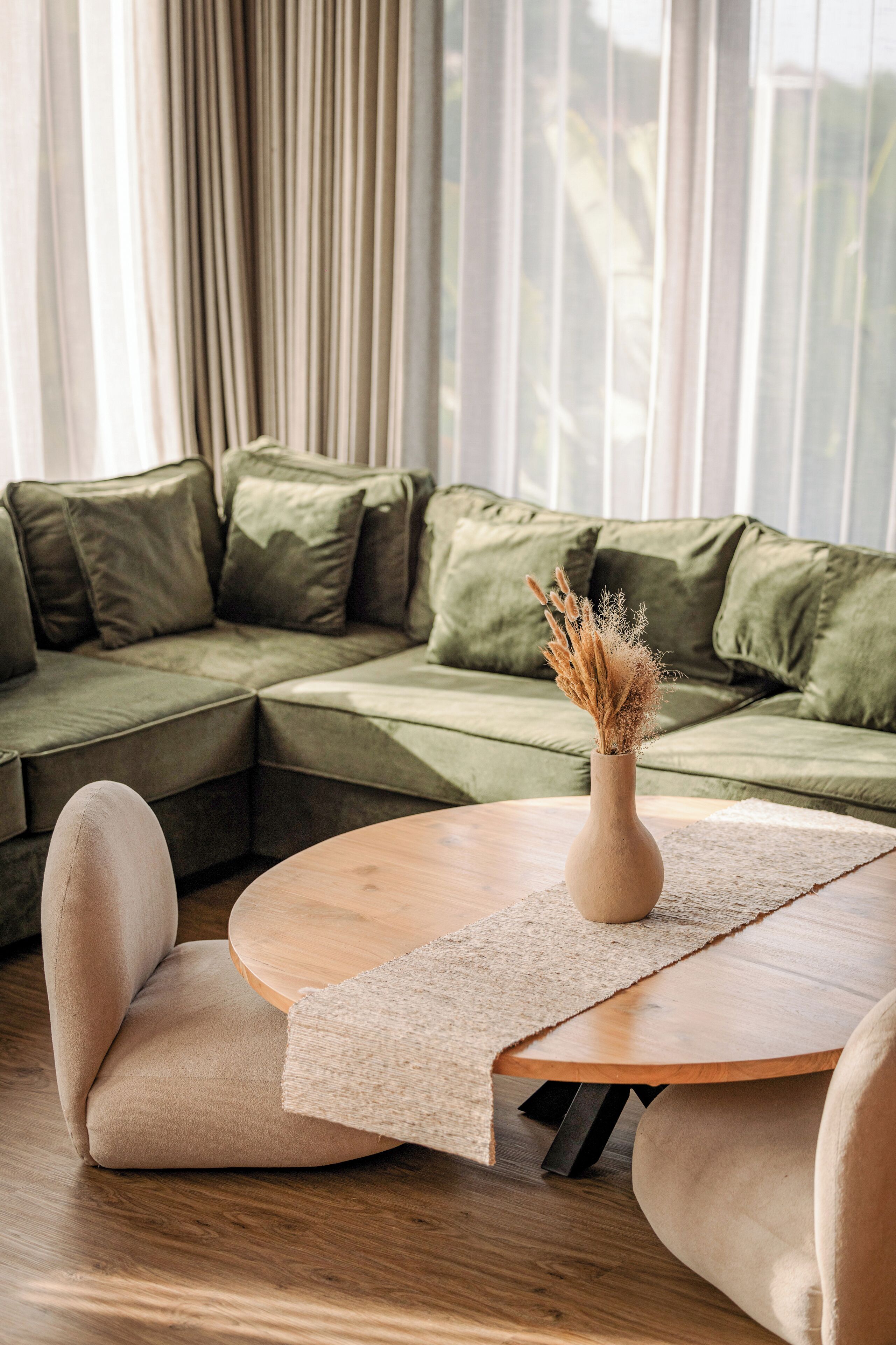 A modern living room with a green sectional sofa, a round wooden coffee table, and a vase with dried plants.