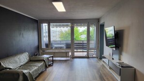 A modern living room with a sofa, a TV, and a sliding glass door leading to a balcony.