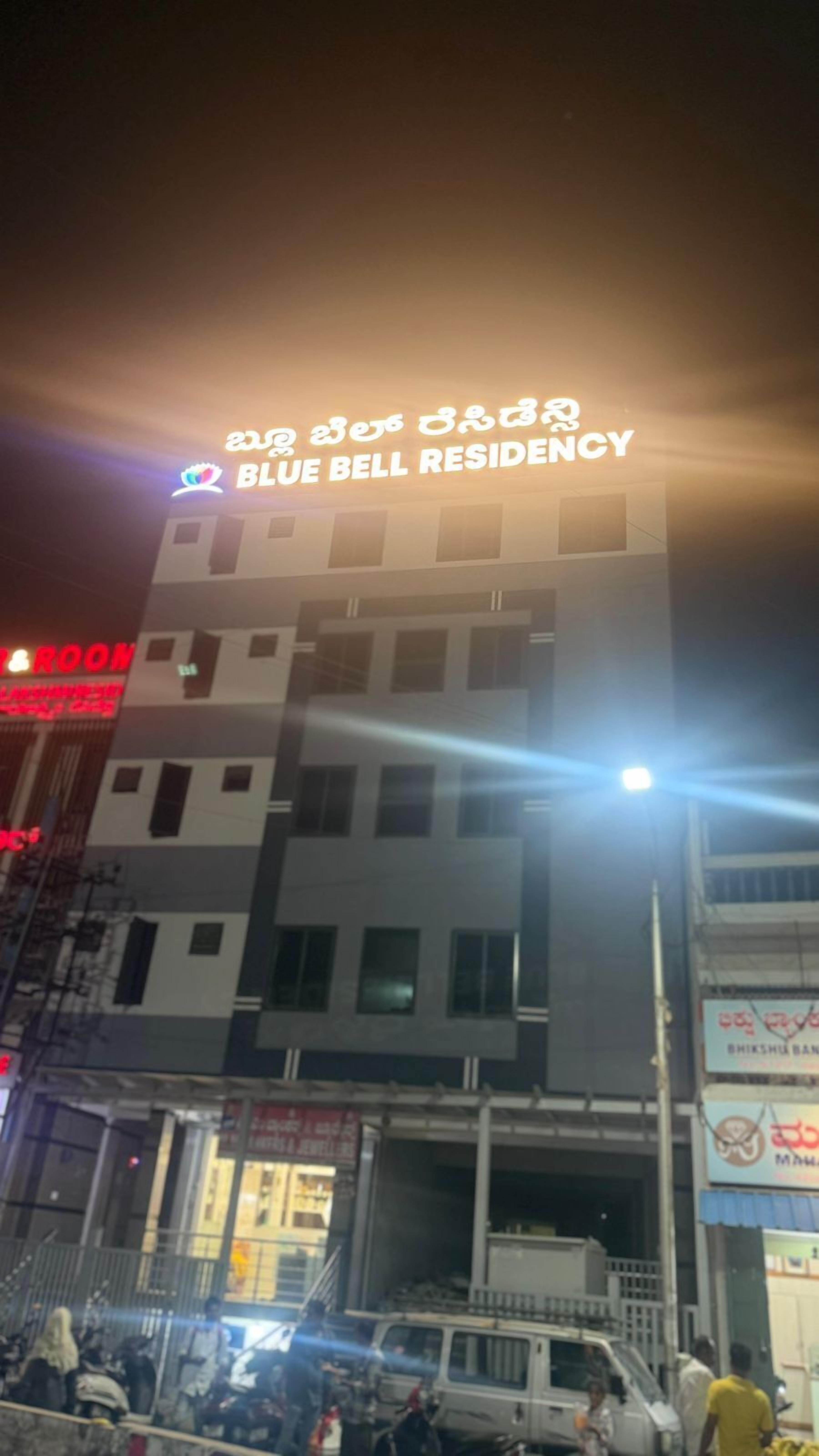 A multi-story building with a sign for "Blue Bell Residency" and various other signs in a foreign language.
