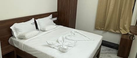 A hotel room with a bed, wooden wardrobe, beige curtains, and a ceiling fan.