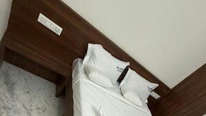 Una cama bien hecha con edredón blanco y almohadas, cabecera de madera y pared de mármol.
