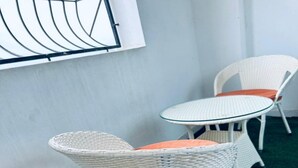 Ein Blick in ein Zimmer, der eine weiße Rattan-Sitzgelegenheit und einen kleinen, runden Tisch mit Glasplatte zeigt.